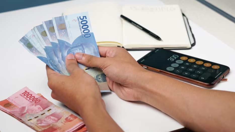 <p>Ilustrasi pelaku usaha menghitung uang tunai hasil pencairan pinjaman. Program pinjaman modal UMKM tanpa agunan ini bisa cair hingga Rp100 juta hanya dengan KTP. Foto: freepik.com</p>
