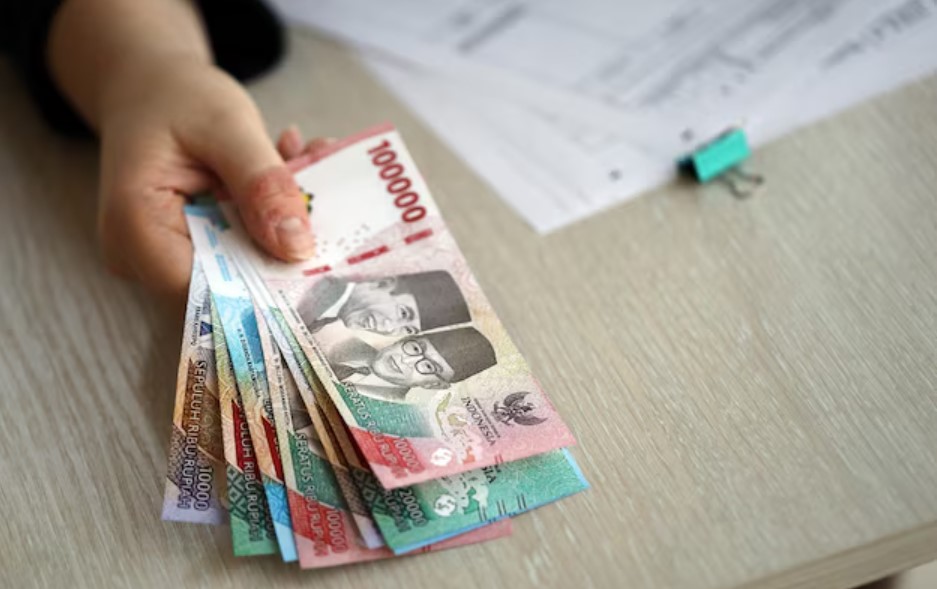 <p>Ilustrasi tangan memegang lembaran uang rupiah, simbol pencairan BPNT Rp600 ribu yang mulai merata di Bank Mandiri dan kini giliran Bank BNI mulai cair bertahap. Foto: freepik.com</p>
